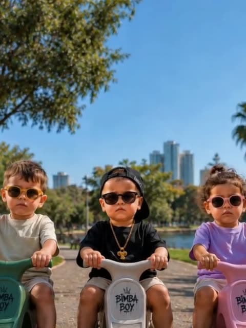 שלושה פעוטות עם משקפי שמש יושבים זה לצד זה על בימבות בפארק הירקון